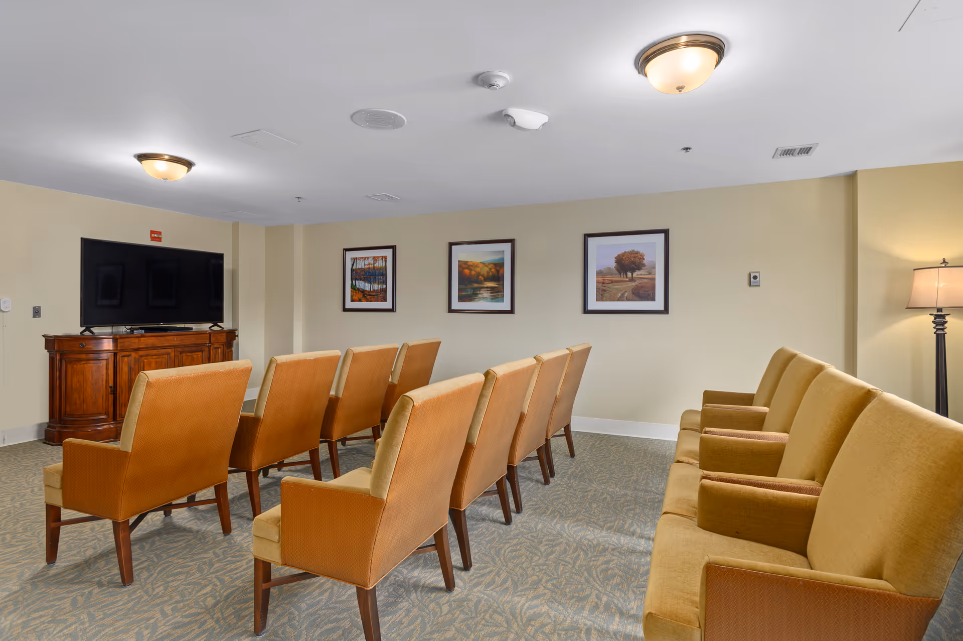 Small theater-style seating area with rows of upholstered chairs facing a television and framed artwork on the wall.