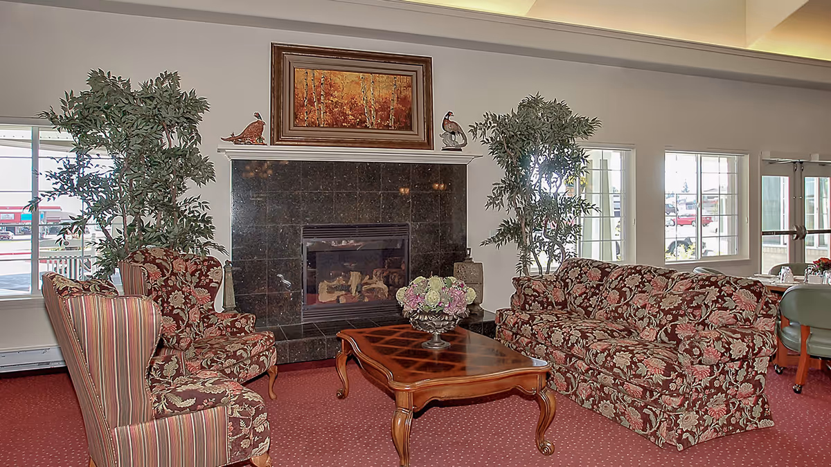 Common room with floral-patterned sofa and chairs arranged around a fireplace and wooden coffee table.