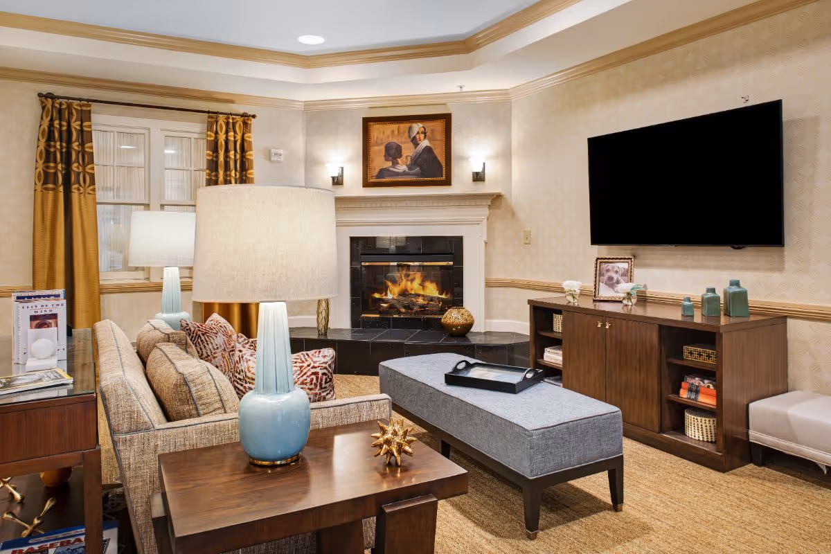 Cozy living room with a sofa, lamps, ottoman, fireplace, wall-mounted TV and wooden console.