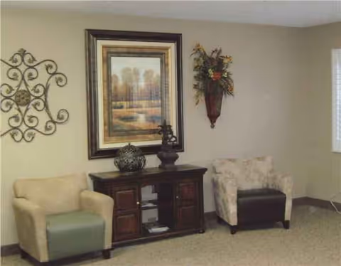 A cozy senior living lounge with two chairs, a dark wood console, and wall decor.