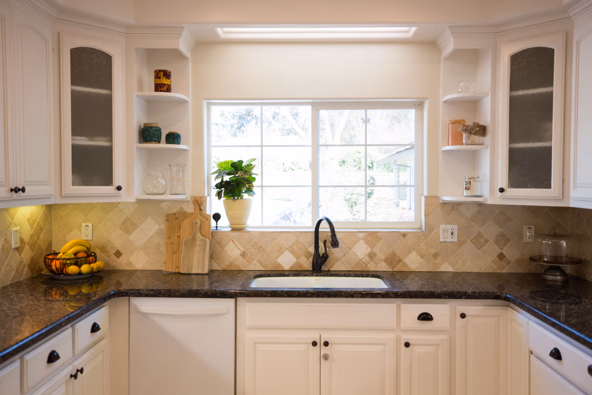 Bright kitchen with white cabinets, a window above a sink, tile backsplash, and dark countertops.