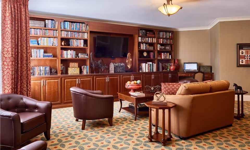 Cozy communal living room with leather chairs, a sofa and coffee table in front of built-in bookshelves and a wall-mounted TV.