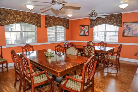 Orange-walled dining room with wooden tables, elegant chairs, and windows.