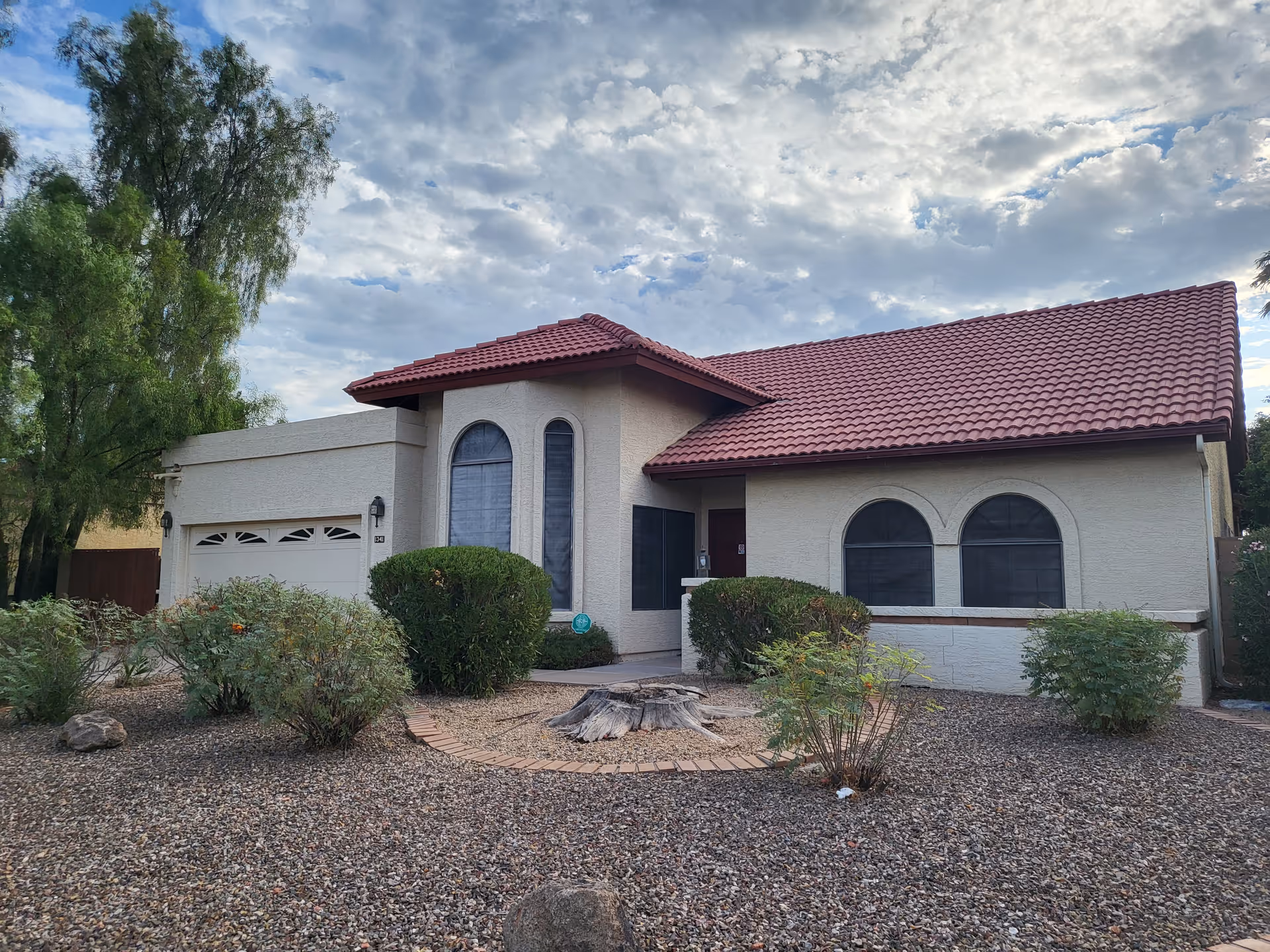 Single-story stucco house with a red tile roof, arched windows, attached garage and desert landscaping in front.