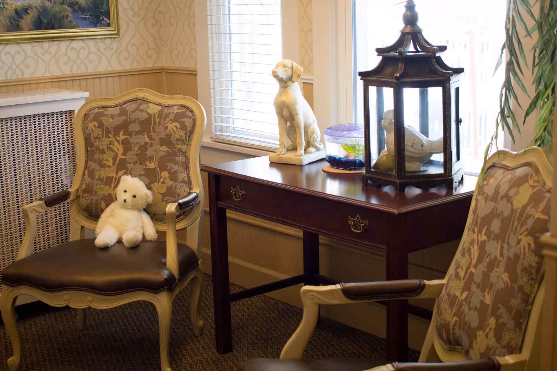 Cozy sitting area with two upholstered armchairs, a small wooden side table topped with decorative sculptures and a teddy bear on one chair.