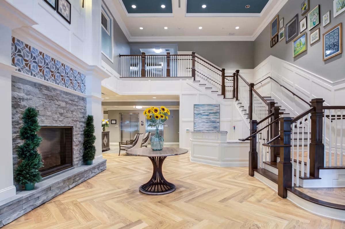 Bright two-story interior lobby with a central table of sunflowers, a stone fireplace, and a sweeping staircase.