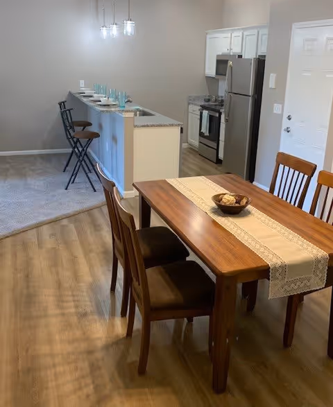 Open-plan dining area with a wooden table and chairs next to a kitchen island with bar stools and stainless steel appliances.