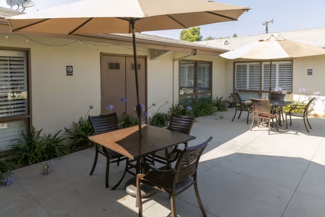Outdoor courtyard patio with tables, chairs, and umbrellas outside a single-story building.