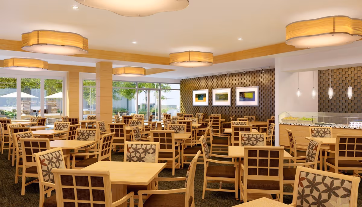 A spacious dining room with multiple wooden tables and chairs featuring patterned cushions. The room has large windows letting in natural light and a view of outdoor umbrellas and greenery. The walls have decorative wood paneling and framed artwork. Modern ceiling lights illuminate the area.