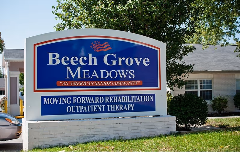 A large outdoor sign for Beech Grove Meadows, an American senior community offering moving forward rehabilitation and outpatient therapy, with a building and greenery in the background.