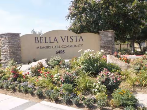 Stone sign reading Bella Vista Memory Care Community amid colorful flowers.