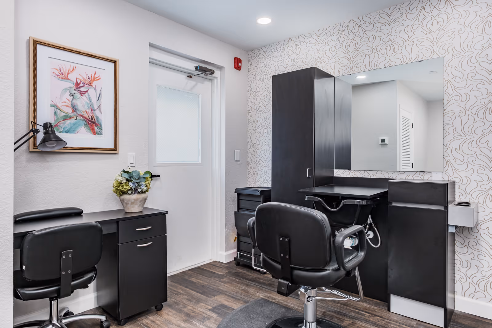 Small interior salon area with black styling chairs, workstations, a mirror and framed artwork.