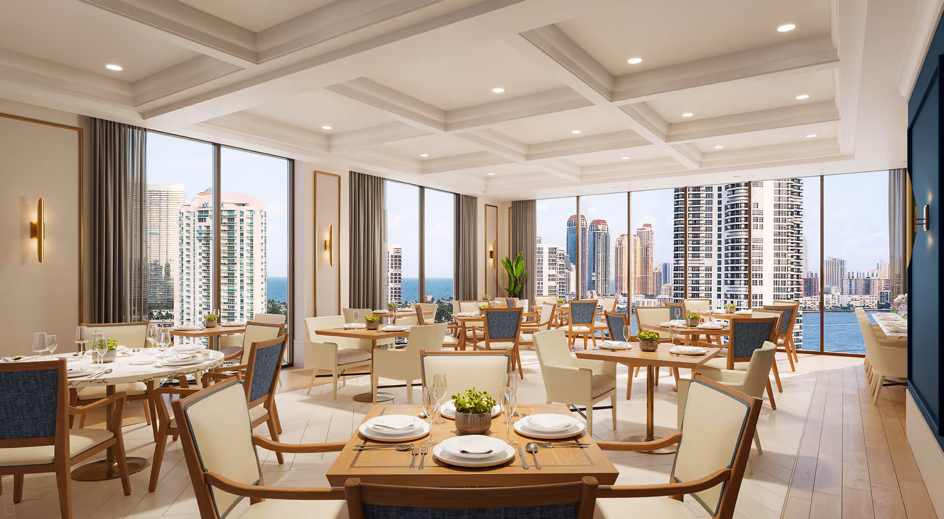 Bright dining room with multiple wooden tables and chairs set with white plates, napkins, and glassware. Large floor-to-ceiling windows offer a panoramic view of a city skyline and water. The room features a coffered ceiling with recessed lighting and modern wall sconces.