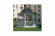 A white gazebo on a grassy lawn with a multi-story building in the background.