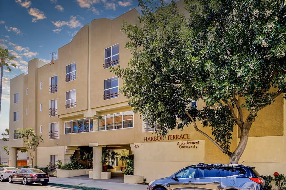 Exterior view of Harbor Terrace Retirement Community building with a tree and parked cars.