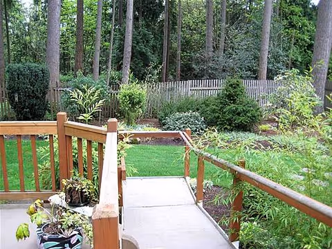 Wooden deck with potted plants leads to a green lawn and garden behind a fence.