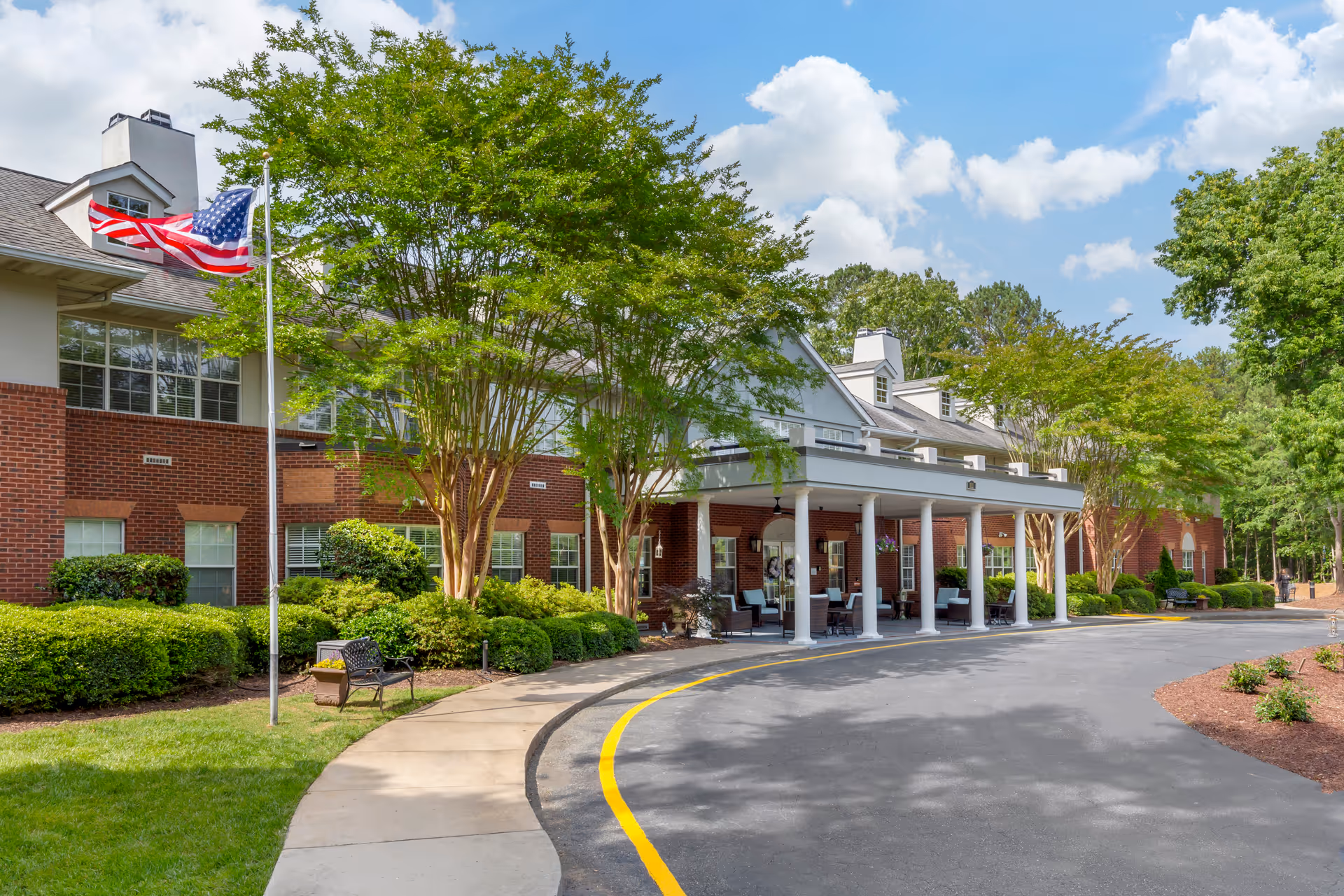 Exterior view of Brookdale MacArthur Park with brick building, flag, and covered entrance.