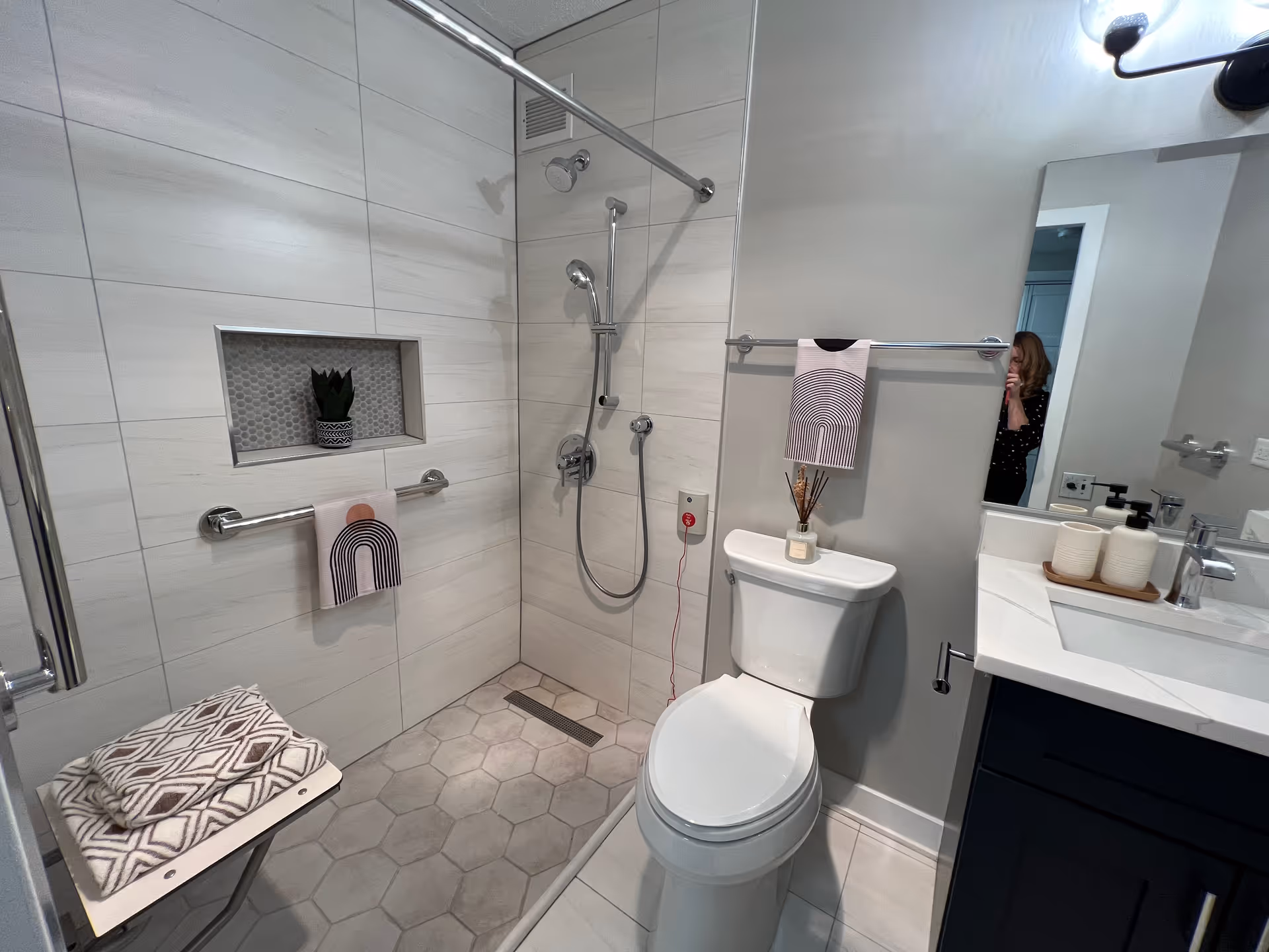Accessible bathroom with a curbless tiled shower, shower seat, grab bars, toilet and sink vanity with towels.
