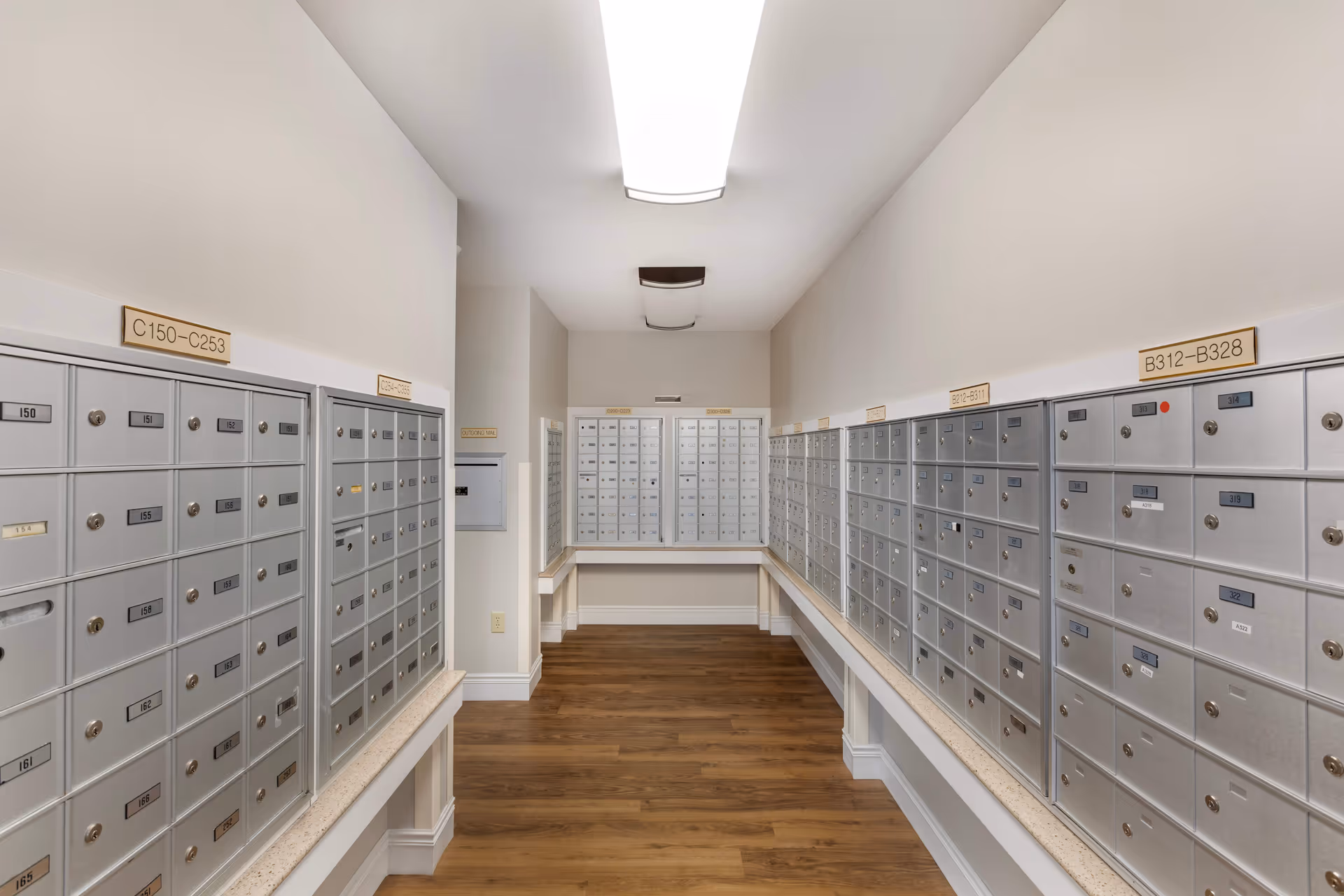 A hallway-style mail room lined with rows of silver mailboxes along both walls and wood flooring.