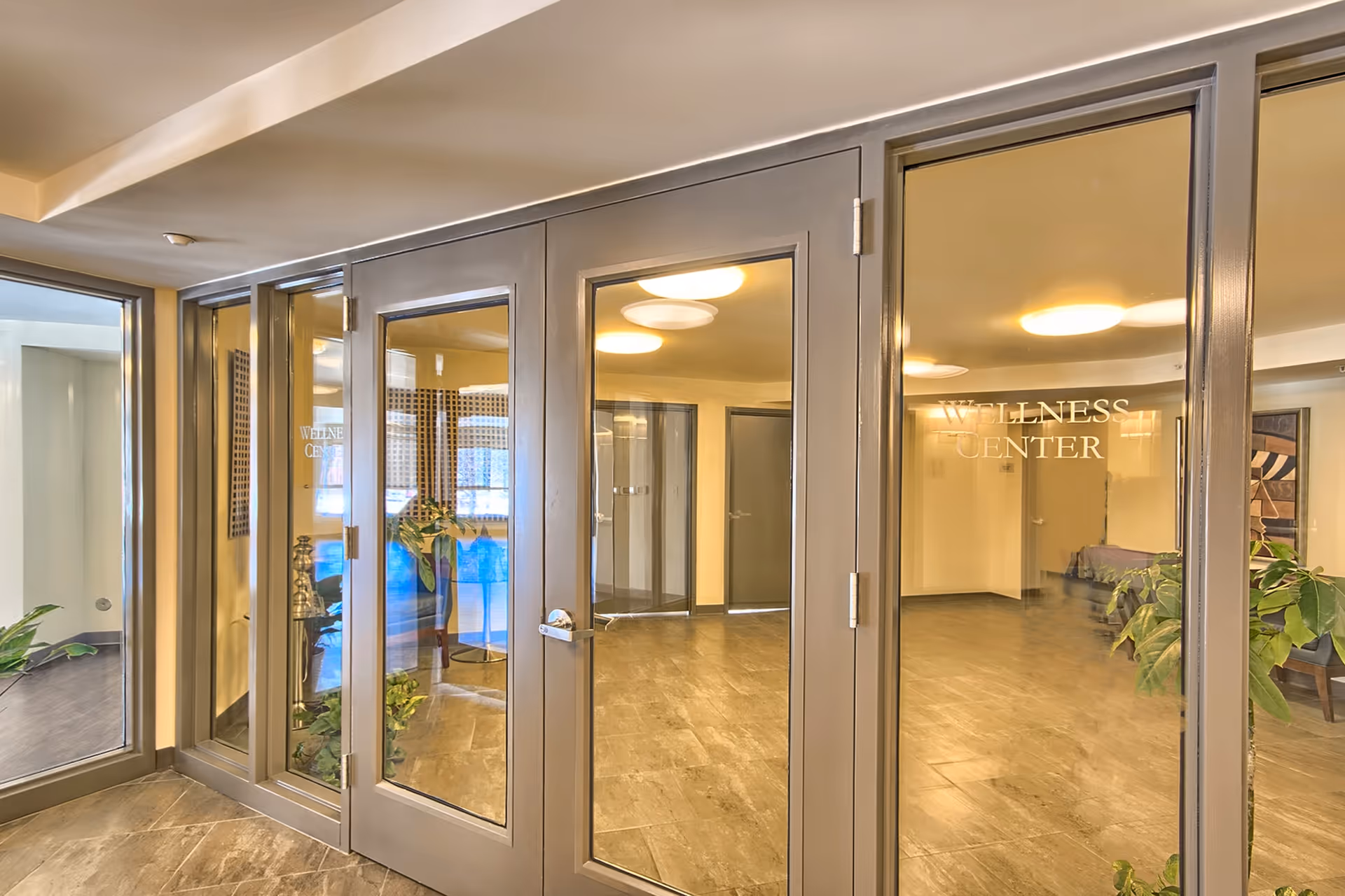 Glass doors and windows with the words 'WELLNESS CENTER' etched on the glass, leading into a well-lit interior space with plants and modern ceiling lights.