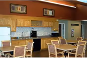 Communal dining area with multiple tables and chairs and a kitchenette featuring cabinets, refrigerator, and microwave.