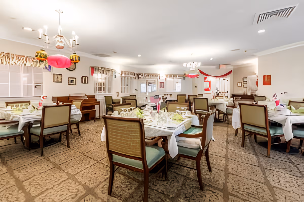 A spacious dining room with multiple set tables and chairs, chandeliers, and festive decorations.