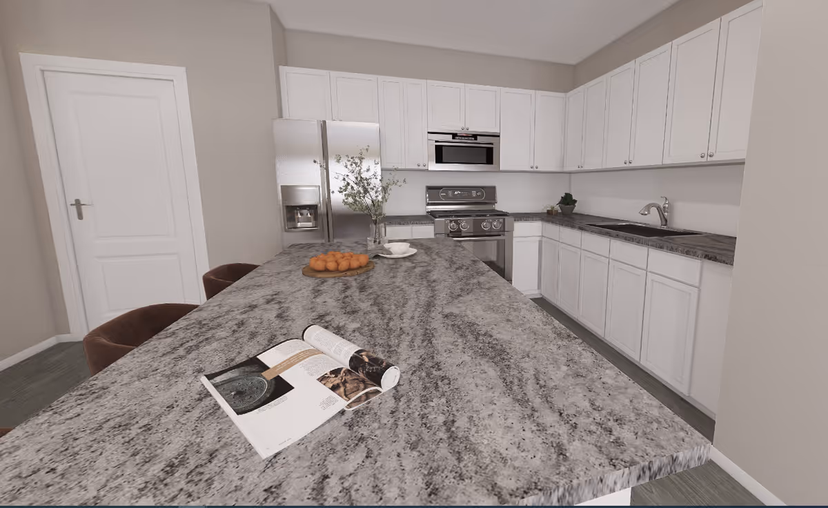 Modern kitchen with white cabinets, a large gray granite countertop island with two brown chairs, a stainless steel refrigerator, stove, microwave, and a sink. There is a vase with flowers, a plate of oranges, and an open magazine on the countertop.