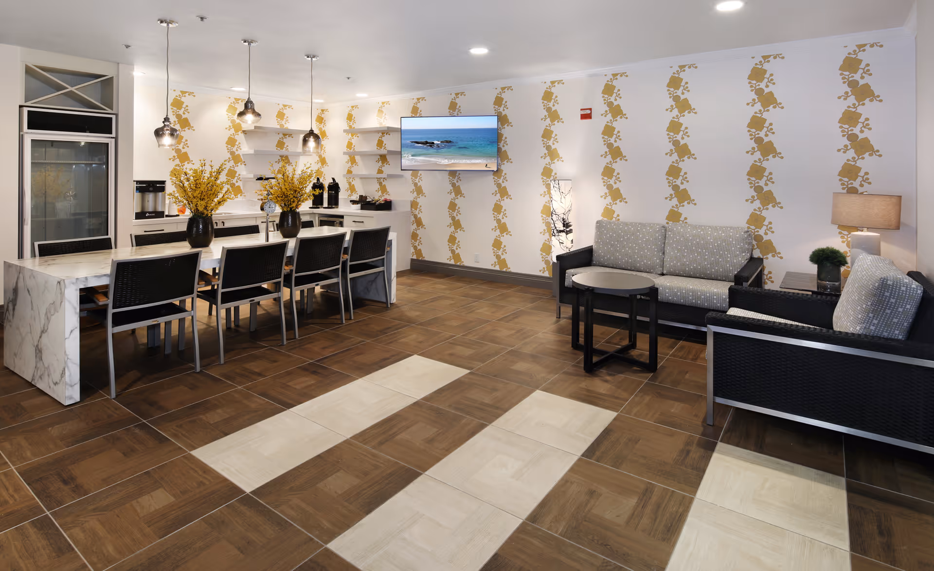 Open communal dining and lounge area with a marble-topped dining island, chairs, sofas, and patterned wallpaper.