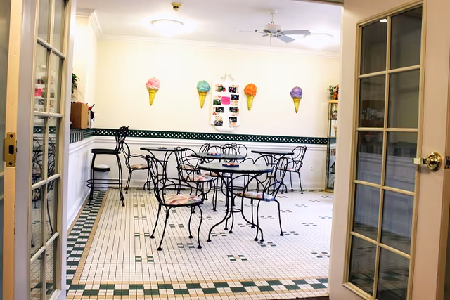 Bright dining room with wrought-iron tables and chairs, ice-cream cone wall decorations, and a tiled floor seen through glass French doors.