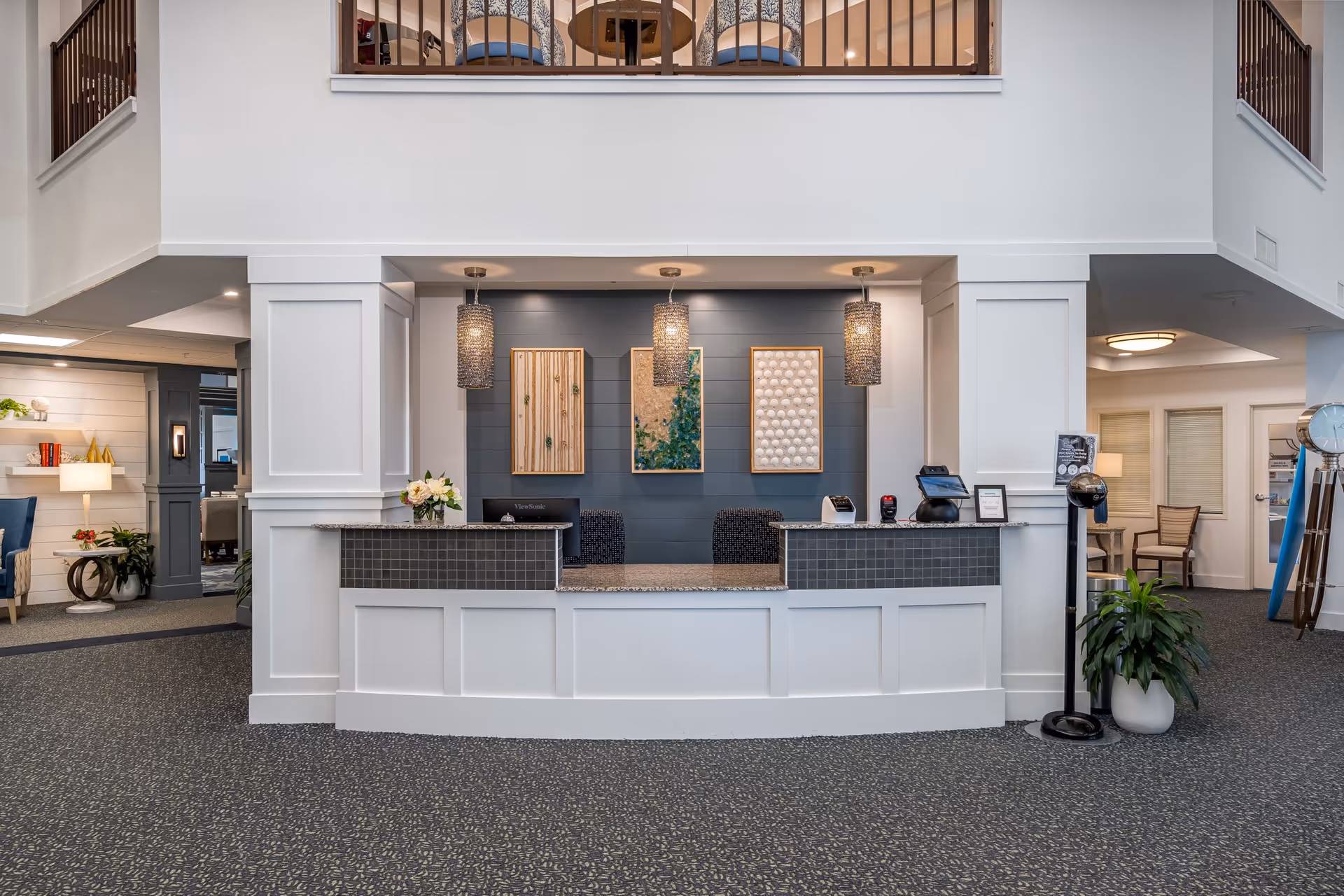 Reception desk and lobby area of a senior living community with pendant lights, artwork, and seating.