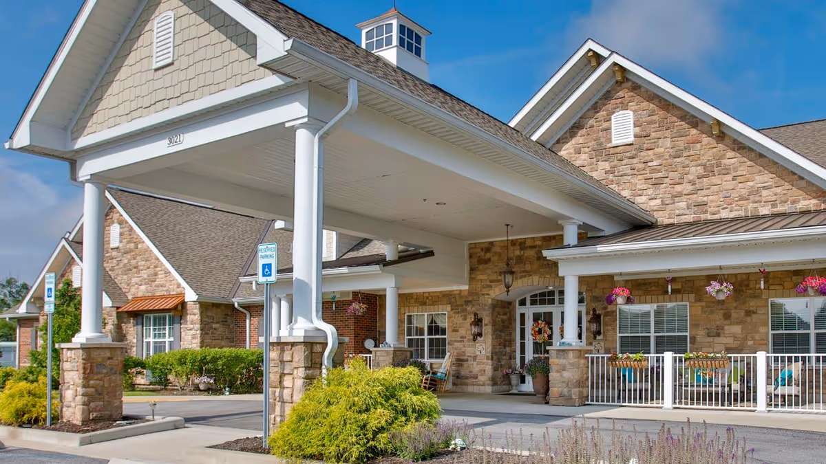 Covered entryway and front porch of a stone-clad building with white columns, hanging flower baskets, and accessible parking signs.