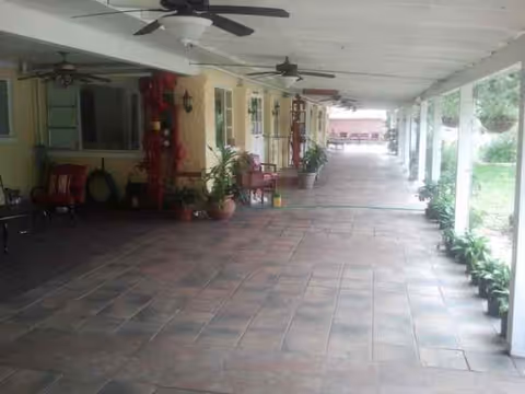 Long covered outdoor patio with ceiling fans, columns, potted plants, chairs, and tiled floor.