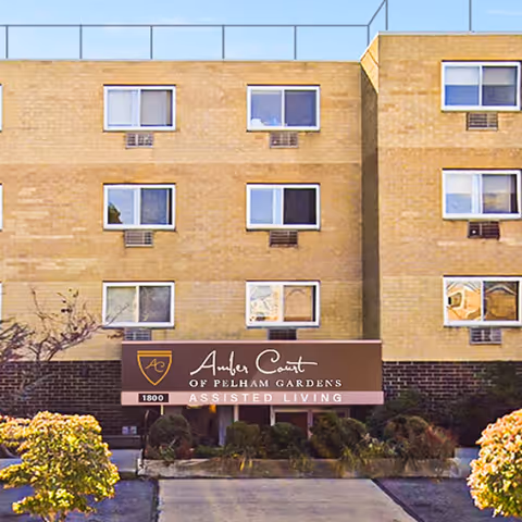 Brick building facade with Amber Court of Pelham Gardens sign and landscaping.