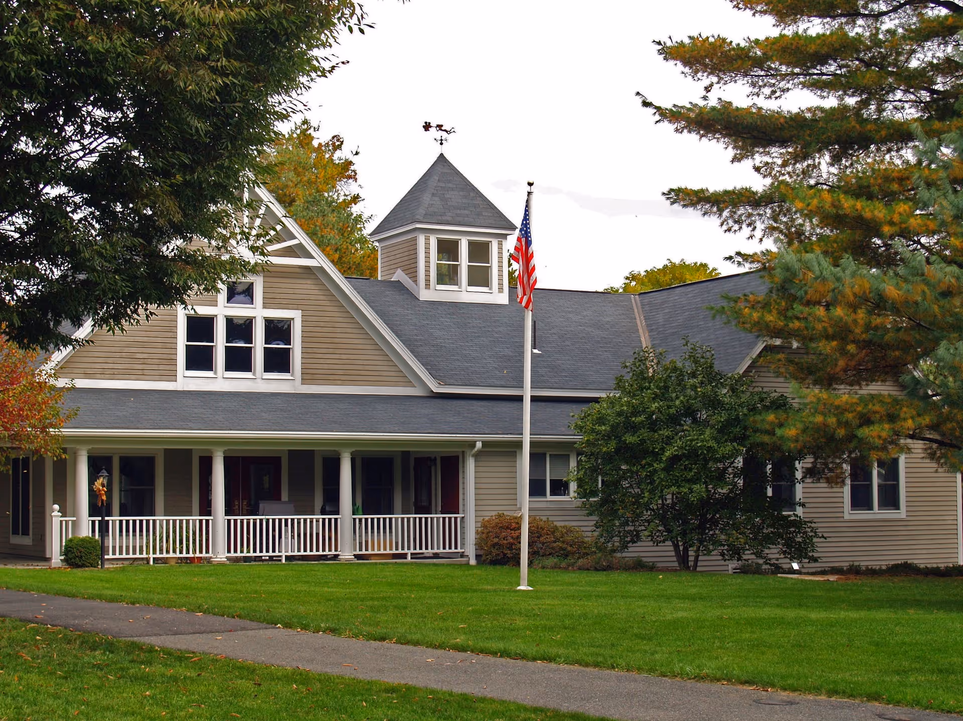 Front exterior of a single-story retirement community building with a covered porch, an American flag on a flagpole, and a green lawn.