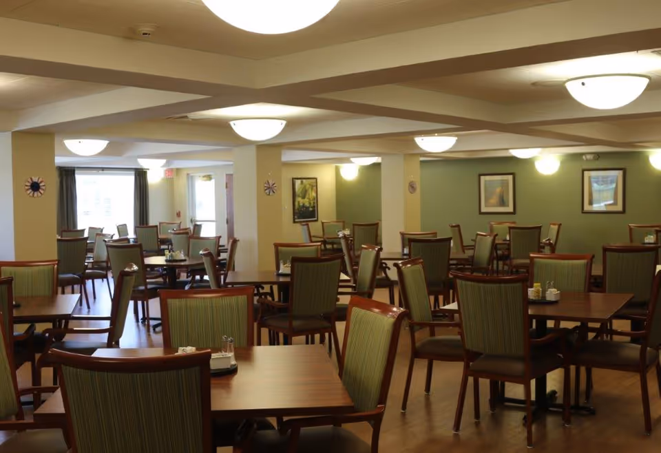 Spacious dining room with multiple wooden tables and green-upholstered chairs under round ceiling lights.
