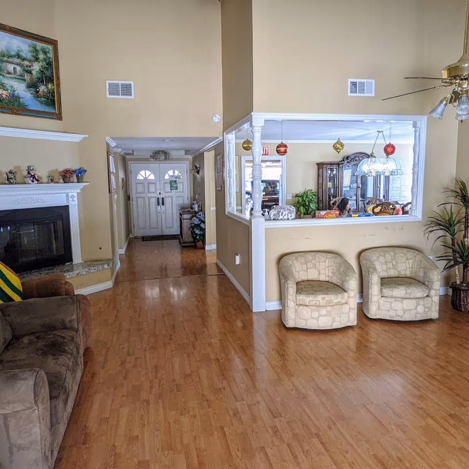 Bright common room with wood floors, seating, a fireplace and the front entrance visible down a short hallway.