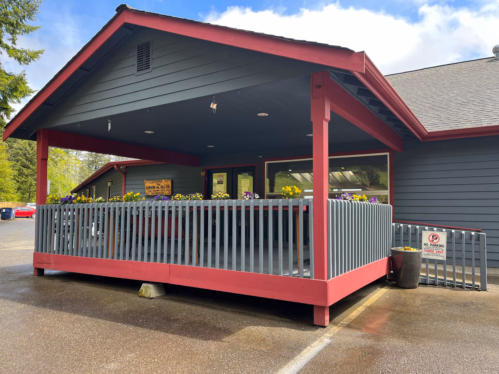 Covered front porch of a gray building with red trim, railings, and flower boxes.