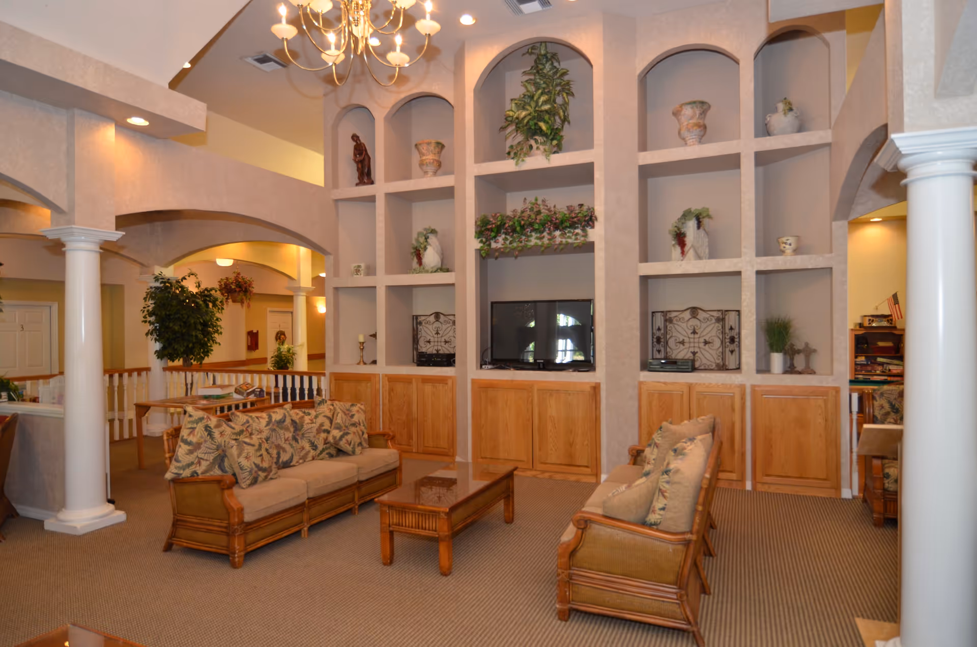 Spacious furnished lounge with sofas, coffee table, built-in shelving, decorative plants and a chandelier.