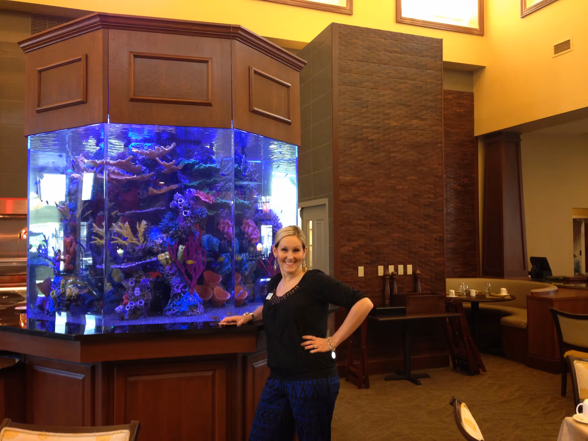 Woman standing next to a large illuminated aquarium in a dining/lounge area.