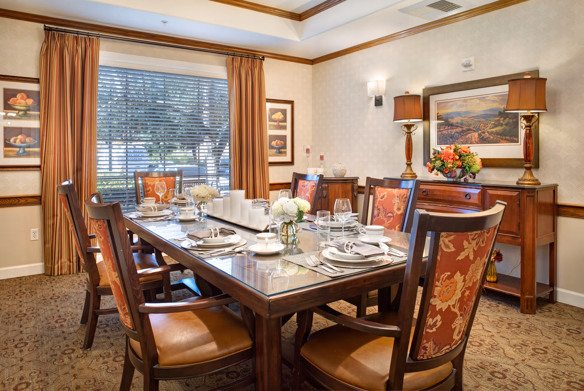 Formal dining room with a set wooden table and upholstered chairs, a sideboard with lamps and flowers, and a large curtained window.