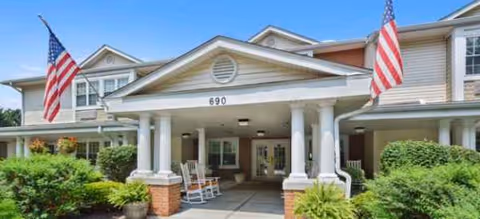 Front entrance of Outlook Manor with white columns, flags, seating, and lush landscaping.