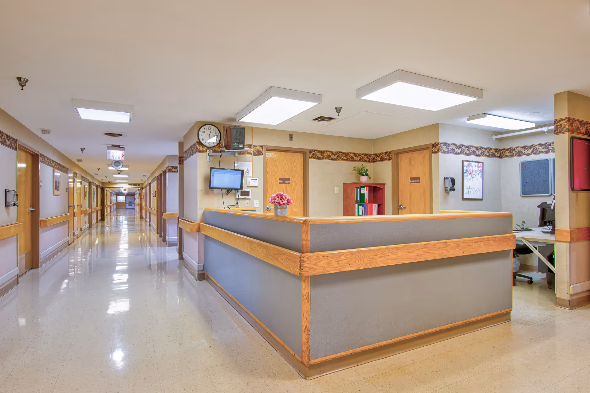 Long interior hallway with a central nurses' station/reception desk in a senior living facility.