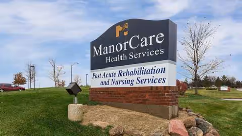 Outdoor ManorCare Health Services sign with rehabilitation text at a landscaped entrance.