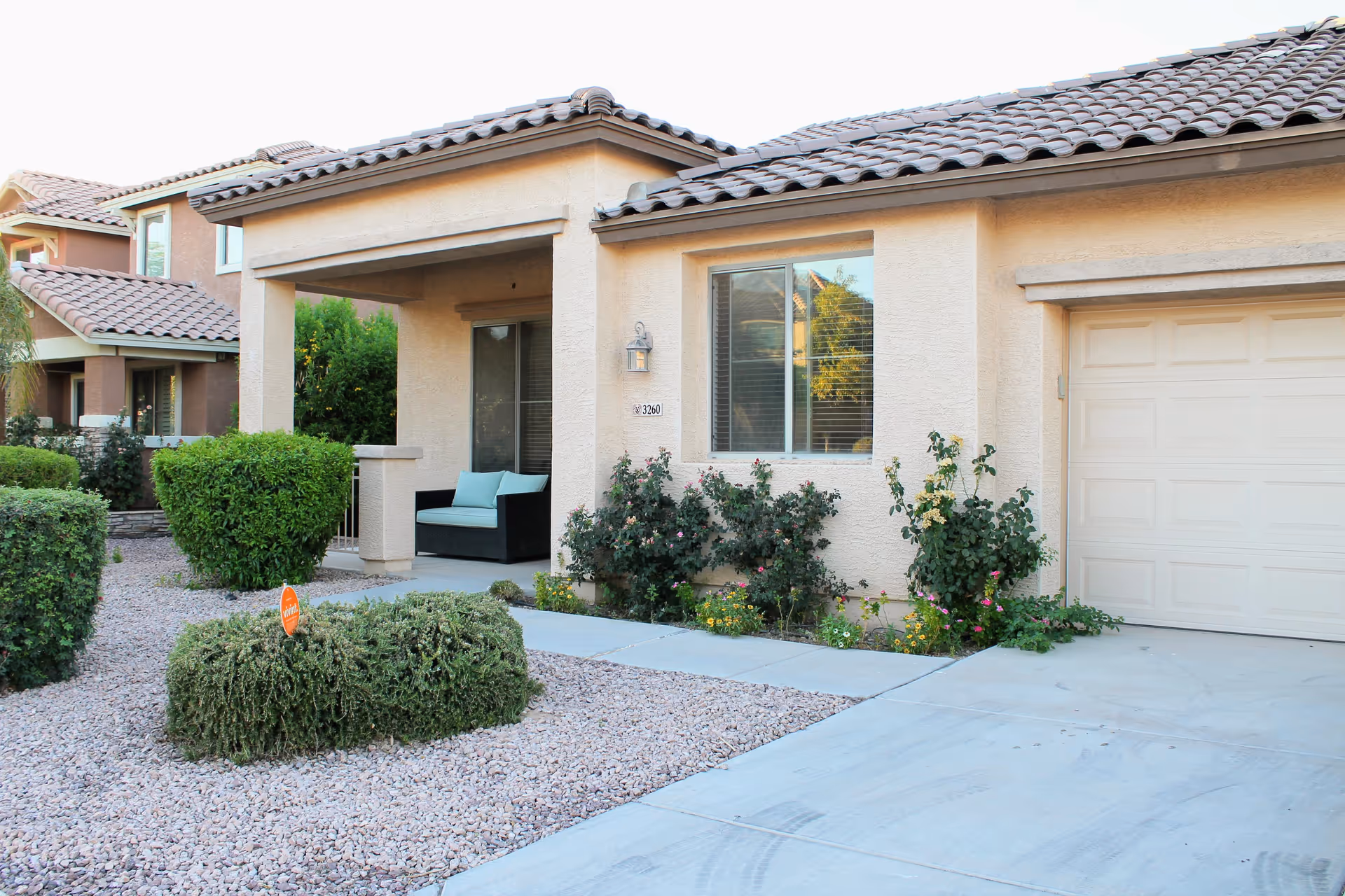 Front exterior of a single-story stucco home with a covered porch, garage, and landscaped gravel yard.