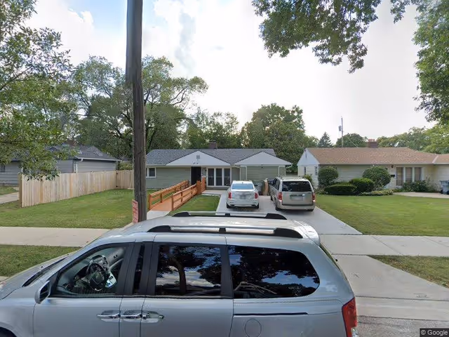 Single-story ranch house with a driveway, three parked cars and a wheelchair ramp leading to the front entrance.