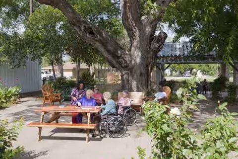 Outdoor courtyard at Towers Nursing Home with seniors gathered at a wooden picnic table.