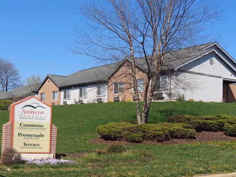 Single-story senior care building on a grassy hill with a foreground sign reading "Amherst Meadows".