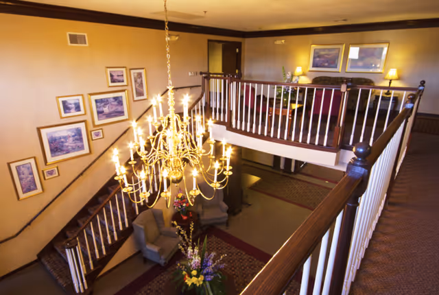 Two-story interior foyer with a large chandelier, staircases, seating areas, framed artwork and floral arrangements.