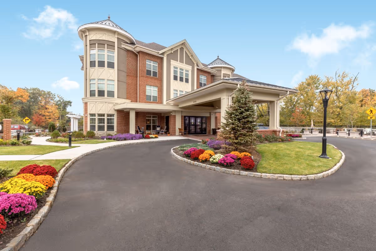 Front entrance of a multi-story brick senior living building with a covered drop-off driveway and landscaped flowerbeds.