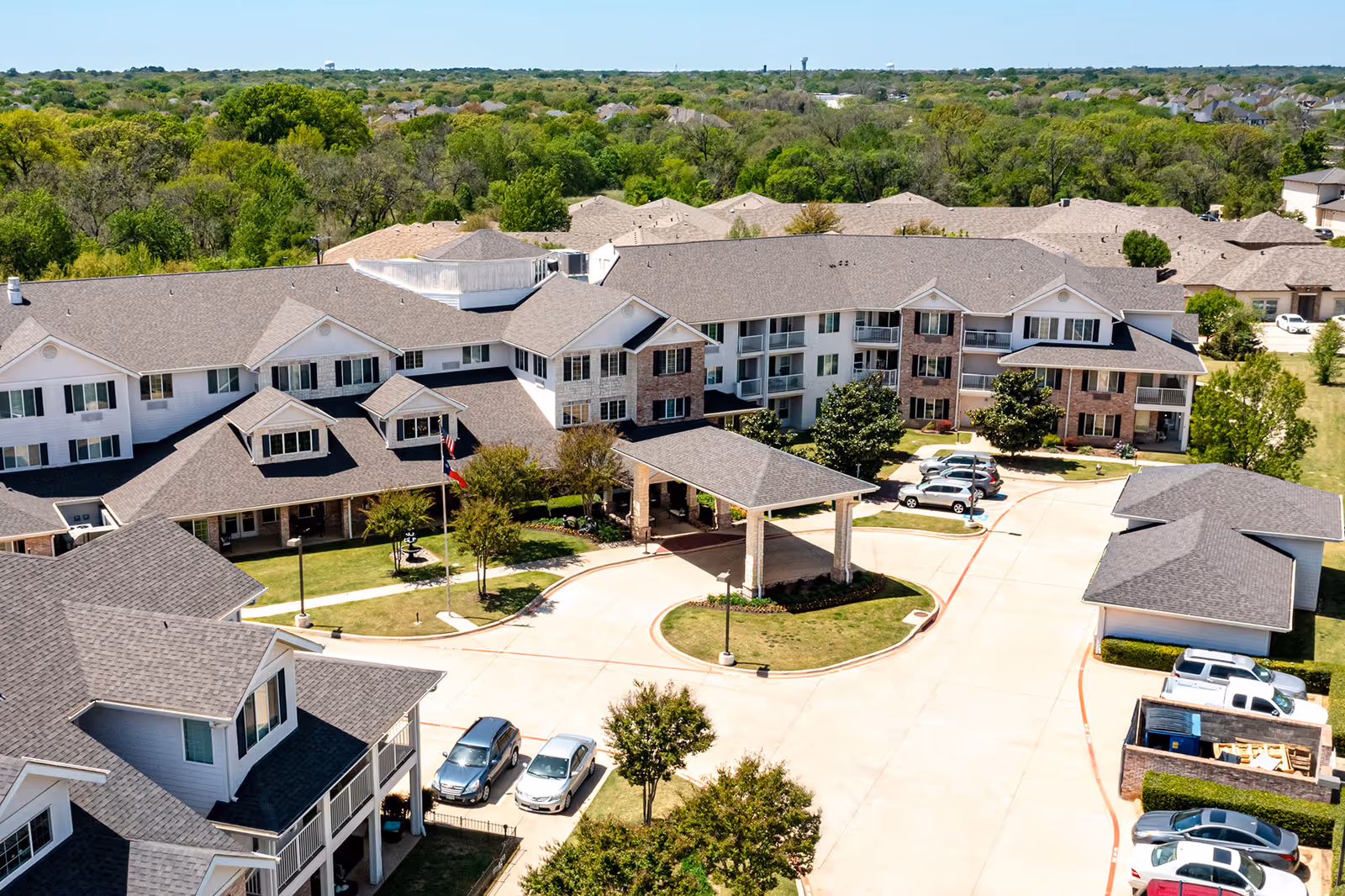 Aerial view of a multi-story senior living facility with a covered entrance, surrounding parking, and landscaped grounds.